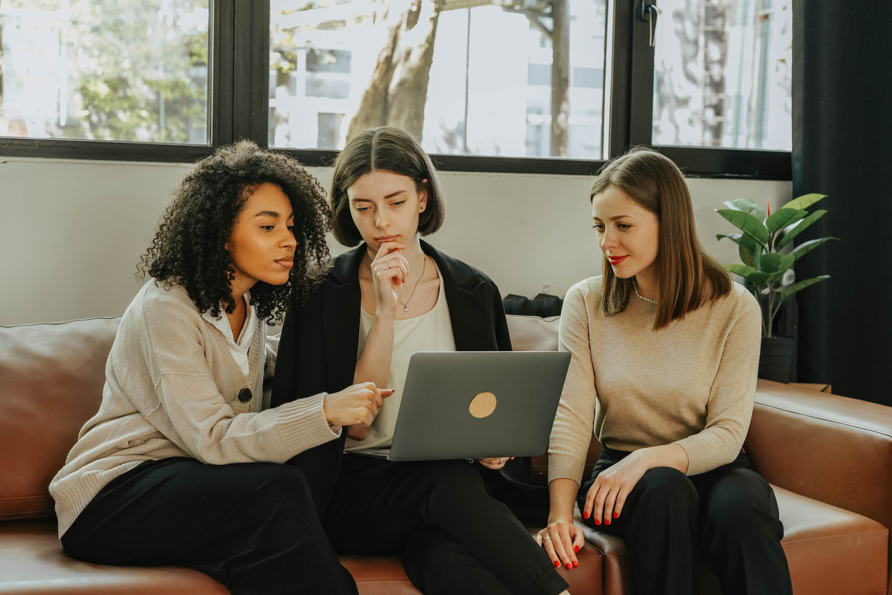 Three Women Sitting on Brown Sofa Looking at a Laptop